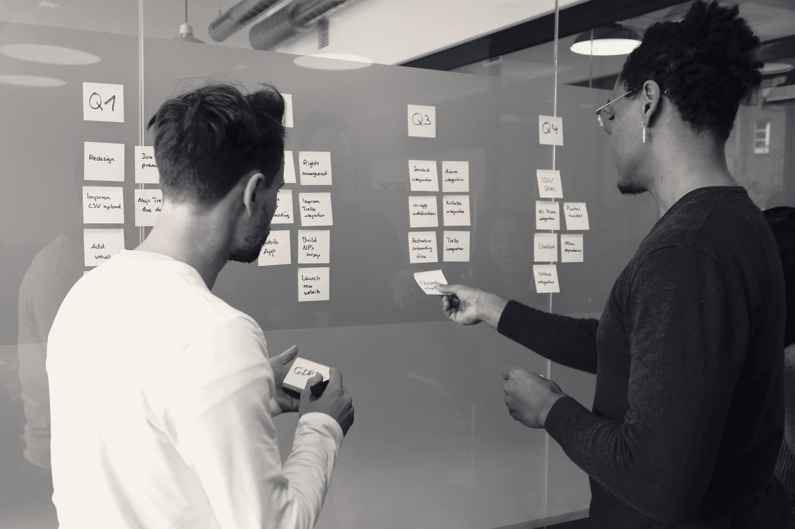 Two people arranging sticky notes on a glass whiteboard