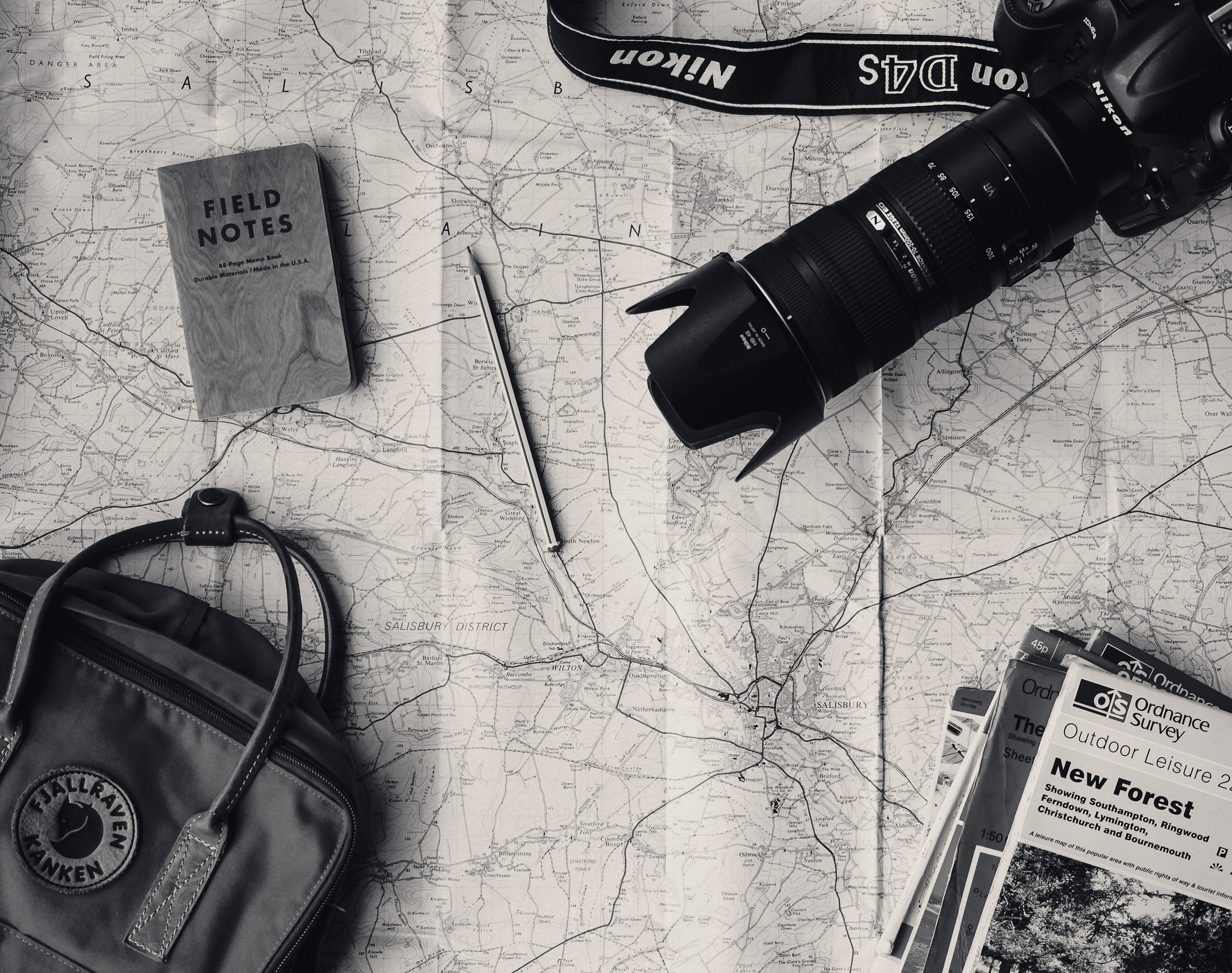Travel map with a camera, notebook and backpack laid out on a table
